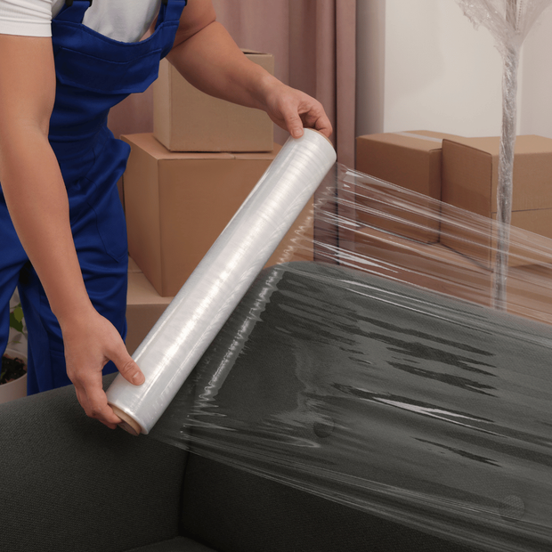 A man is wrapping a couch with plastic wrap