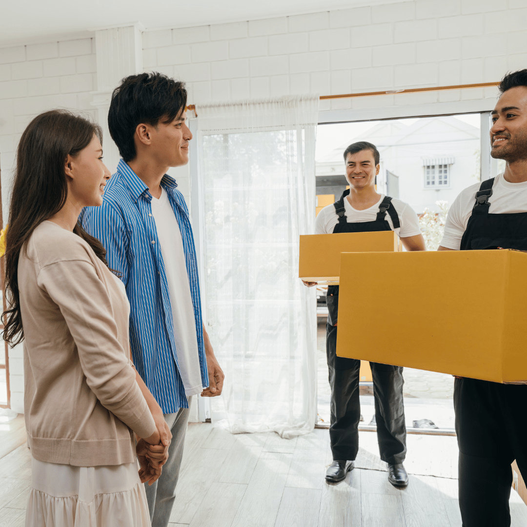 A group of people are standing in a living room talking to a man holding a box.