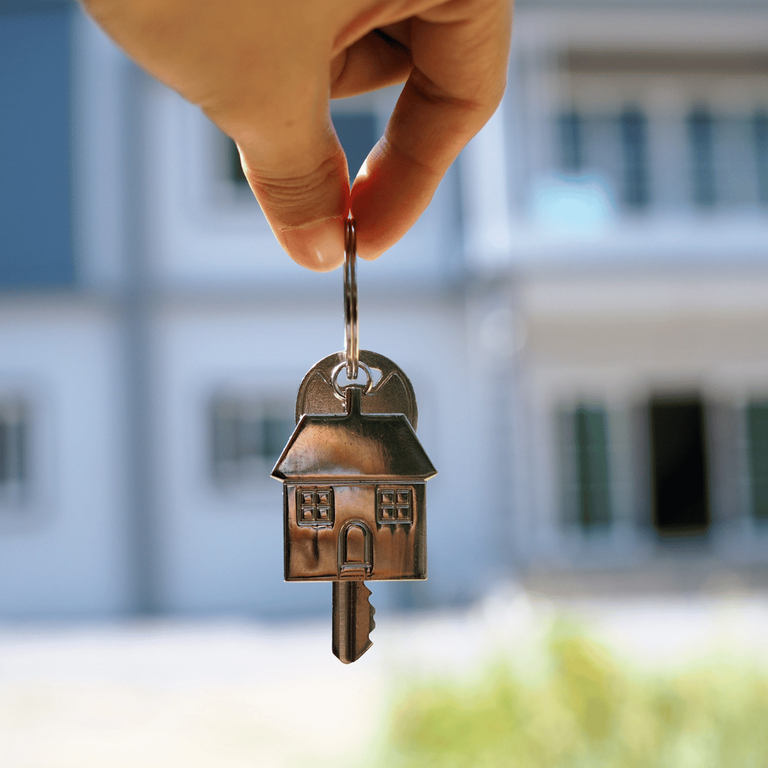 A person is holding a house key in front of a house