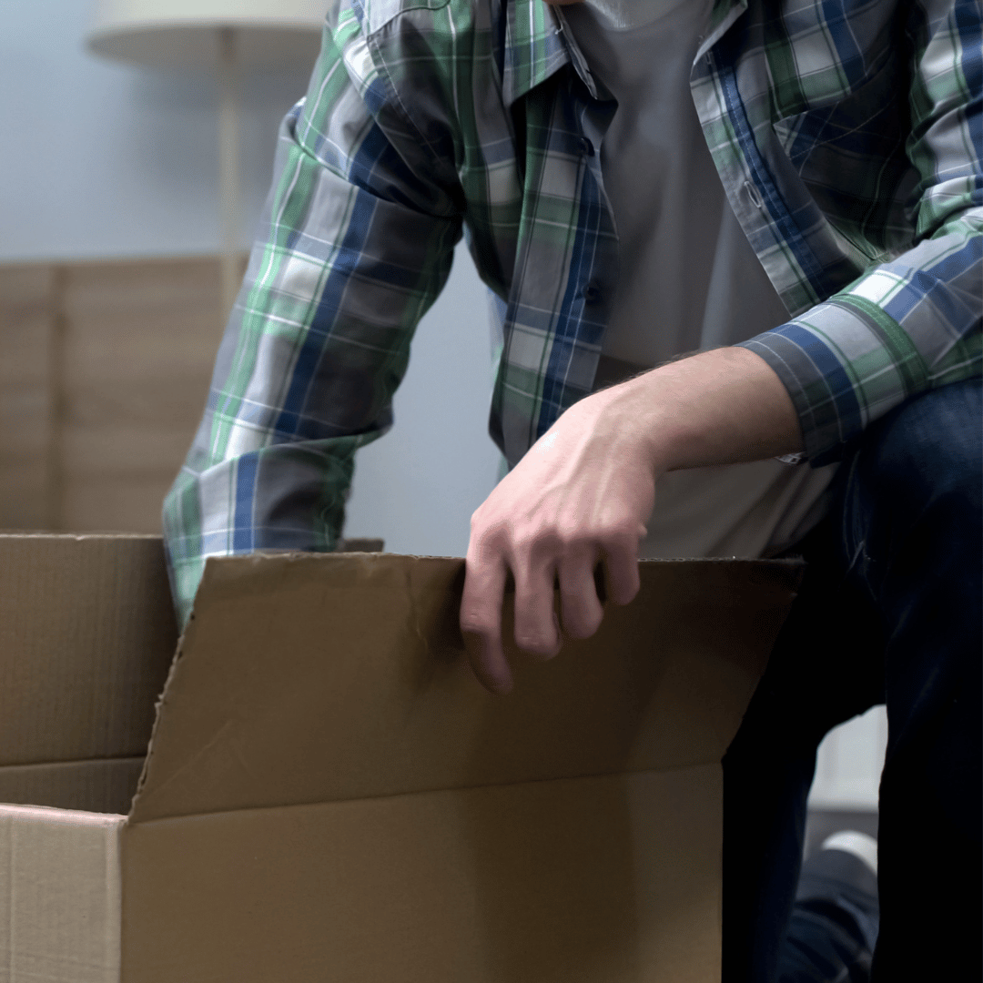 A man in a plaid shirt is opening a cardboard box.