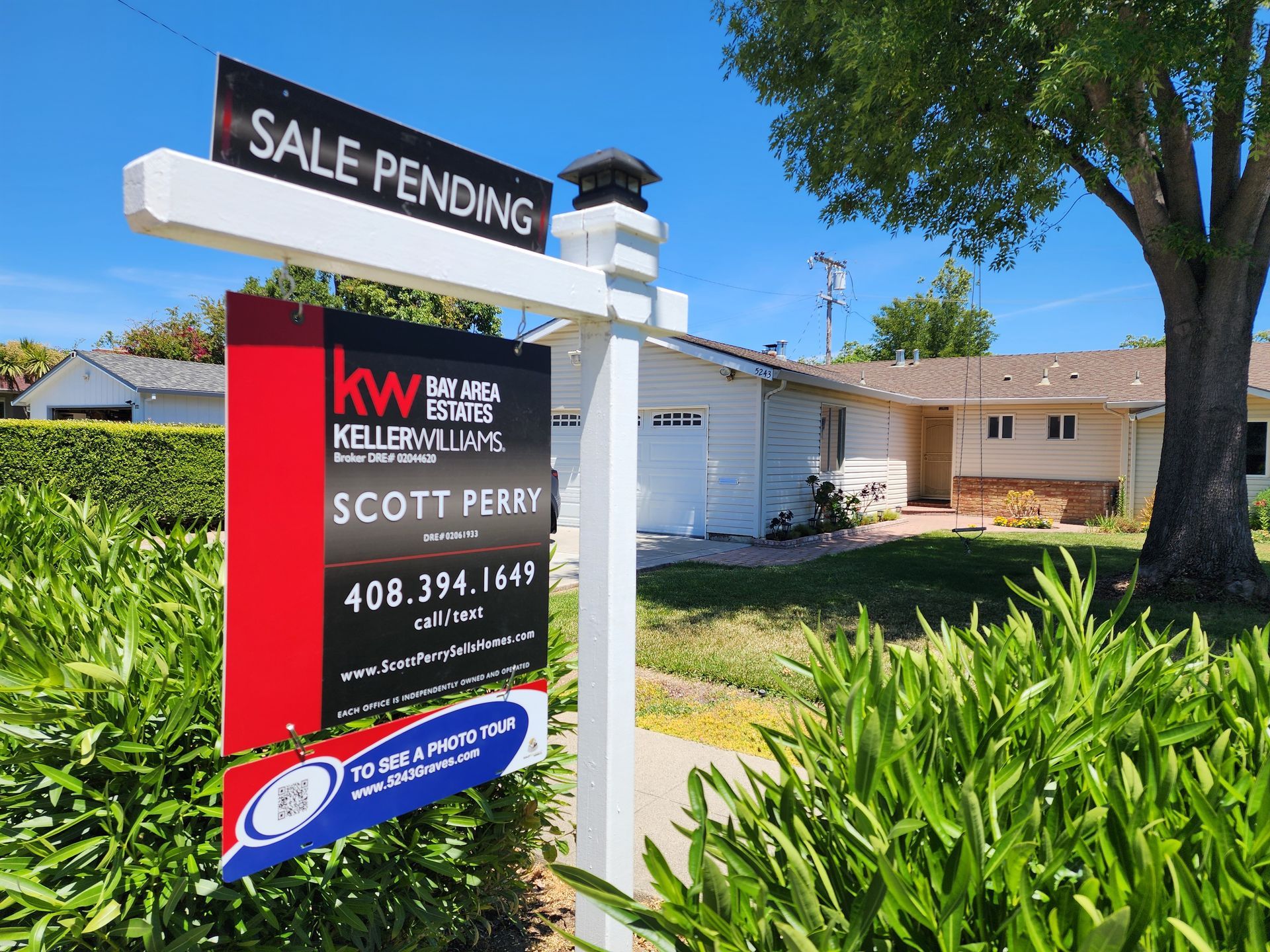 House with blue and white exterior, green lawn, trees, and bright blue sky.