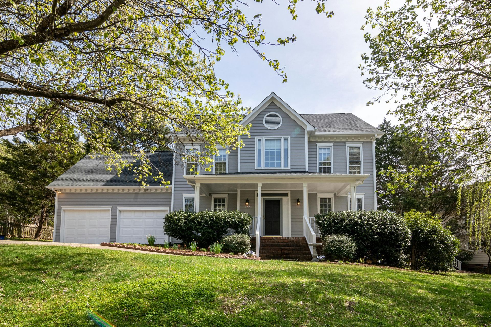 House with blue and white exterior, green lawn, trees, and bright blue sky.