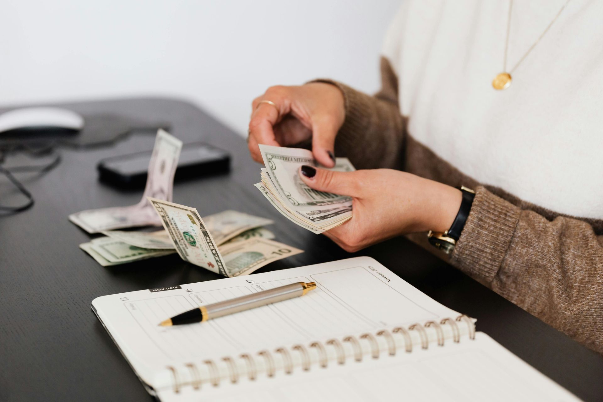 Person counting cash at desk with notebook and pen