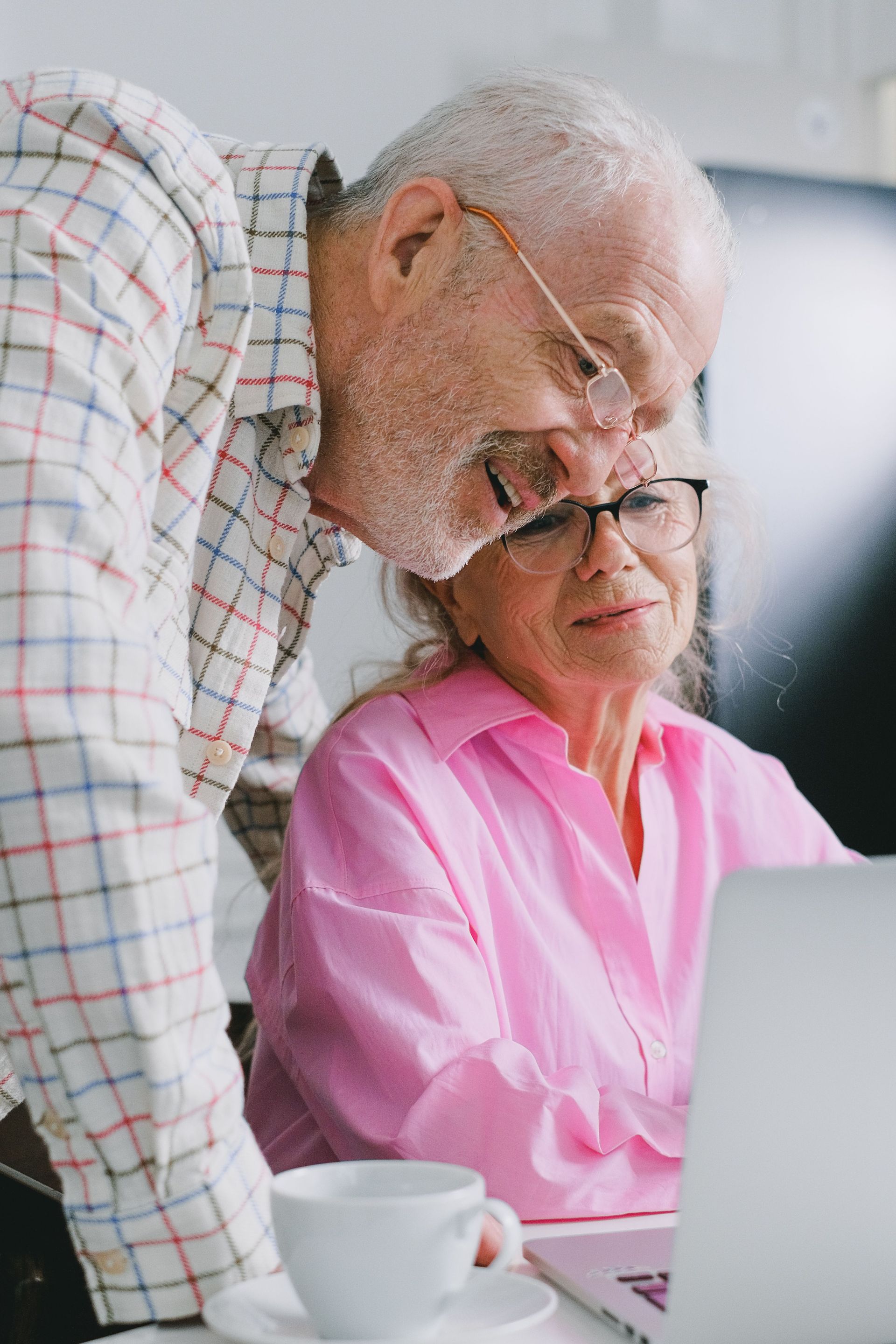 Older couple looking at a laptop in a bright office, with a white coffee cup nearby