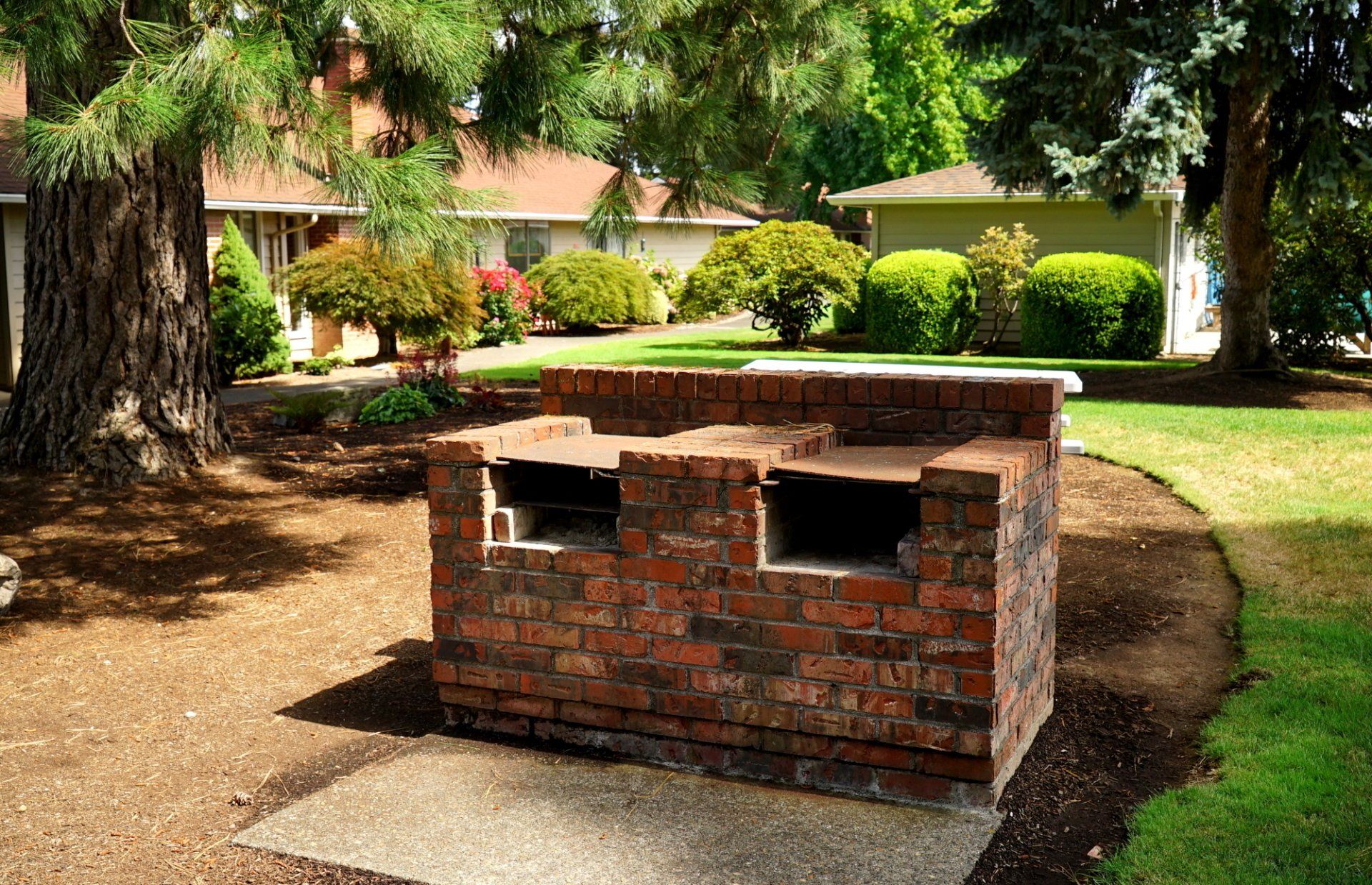 A brick grill is sitting in the middle of a lush green yard.