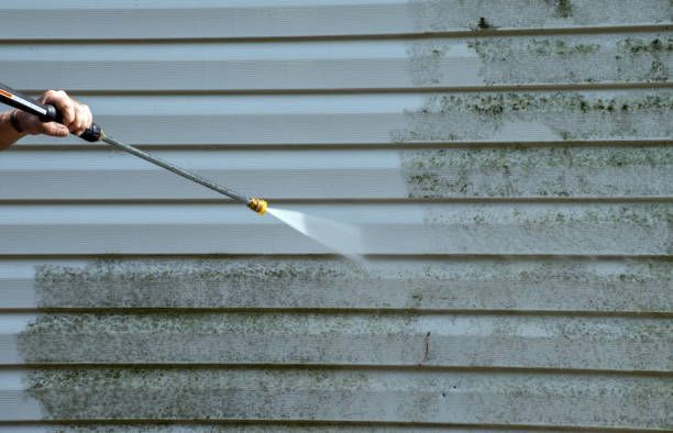Person pressure-washing dirty gray siding with a spray wand