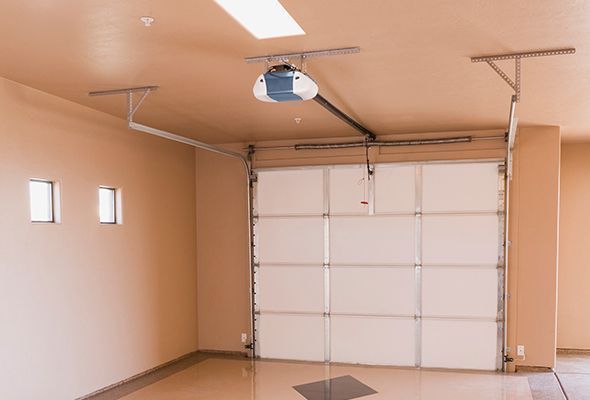 Empty beige garage with a closed white sectional door and ceiling-mounted opener.