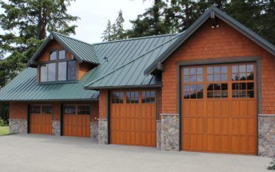 Large modern garage with orange wood doors, stone accents, and green metal roof