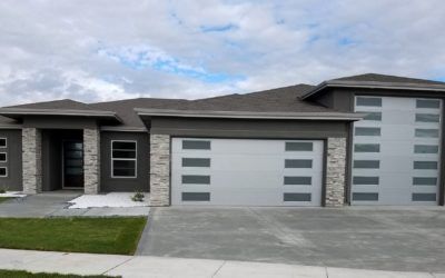 Modern gray suburban house with three-car garage and driveway under a cloudy sky