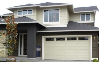 Suburban two-story house with light siding, dark roof, and a cream-colored garage door.