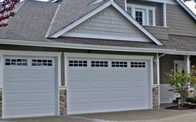 Two white garage doors on a suburban house with gray siding and a shingled roof