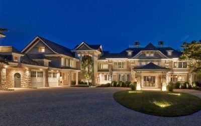 Large stone mansion at dusk with warm lights, a circular driveway, and manicured landscaping