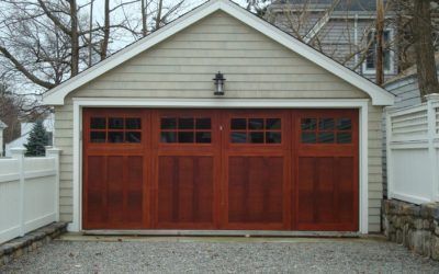 Red wooden garage door on a house with white siding and stone side walls.
