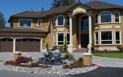 Large beige two-story house with arched windows, three-car garage, and landscaped rock garden in front