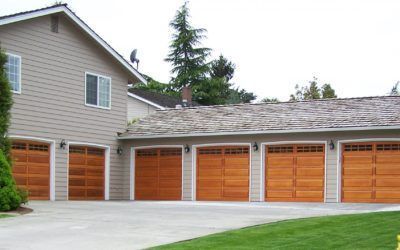 Row of three orange garage doors on a light gray house with a paved driveway and trees around it