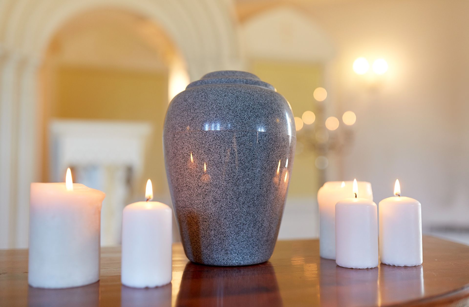 Gray urn and lit candles on a wooden table in a softly lit room.
