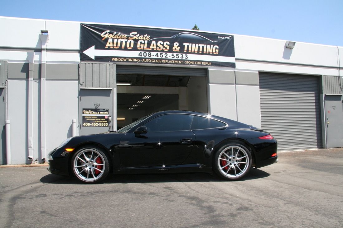 A black sports car is parked in front of a building that says auto glass and tinting