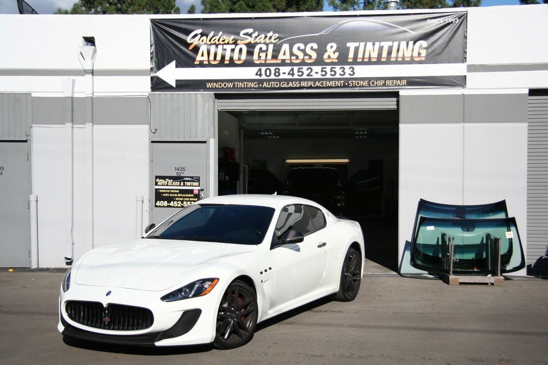 A white car is parked in front of a building that says auto glass and tinting.