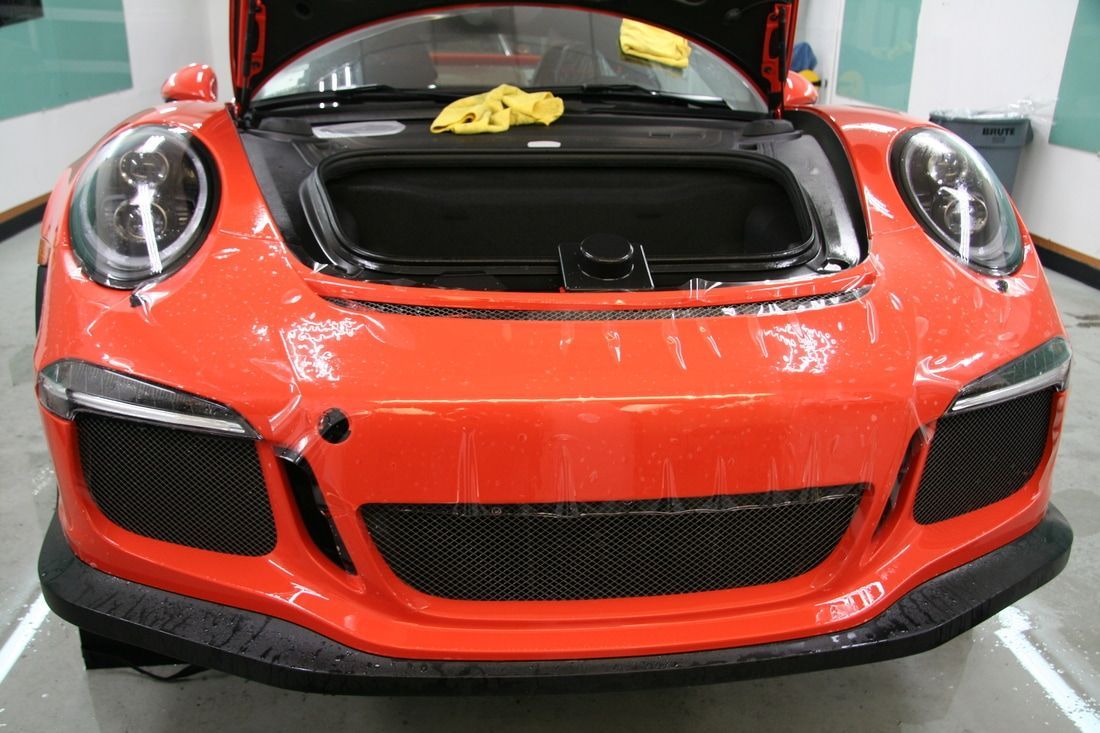 A red sports car with the hood open is sitting in a garage.