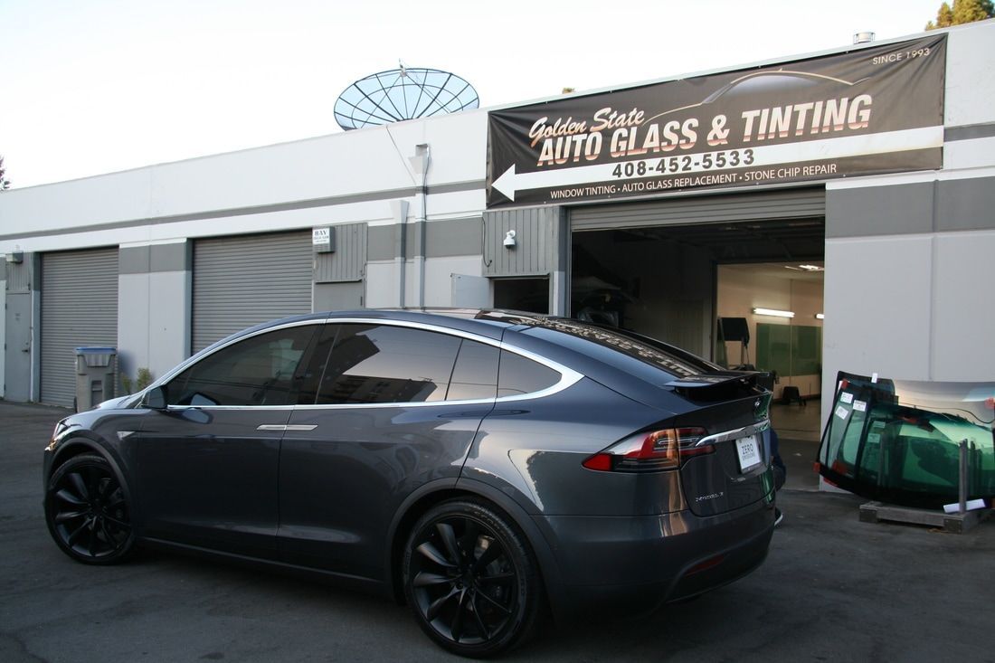 A gray car is parked in front of a building that says auto glass and tinting