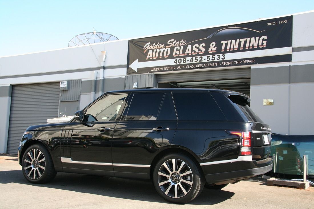 A black range rover is parked in front of a building that says auto glass and tinting