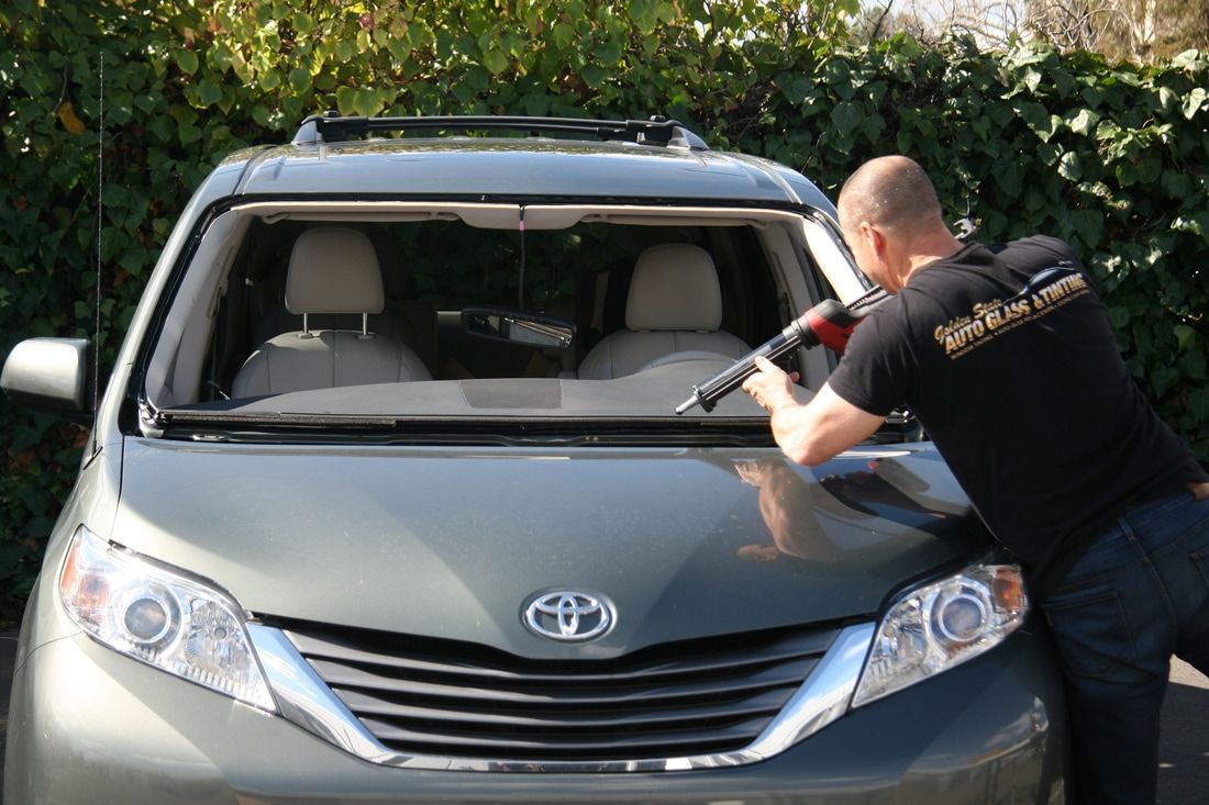 A man is installing a windshield on a toyota sienna.