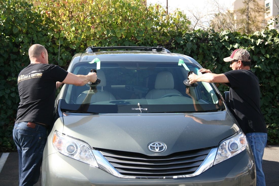 Two men are installing a windshield on a toyota sienna.