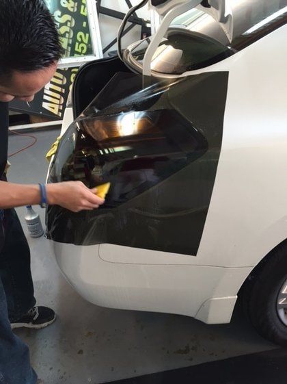 A man is working on a white car with a sign in the background that says auto glass