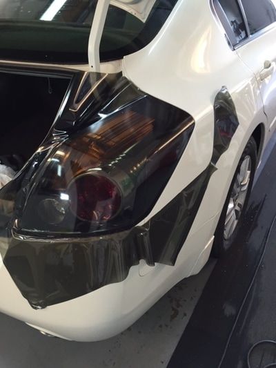 A white car is being wrapped in black plastic