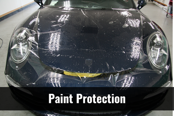 A black car is covered in plastic and the words paint protection are above it