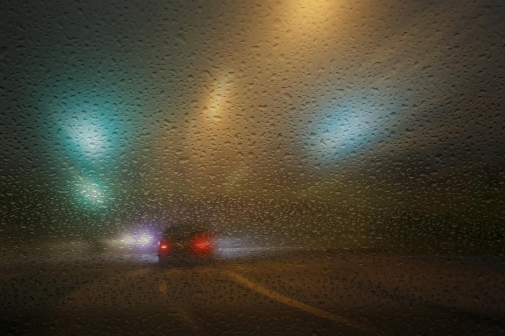 A car is driving down a highway at night in the rain.