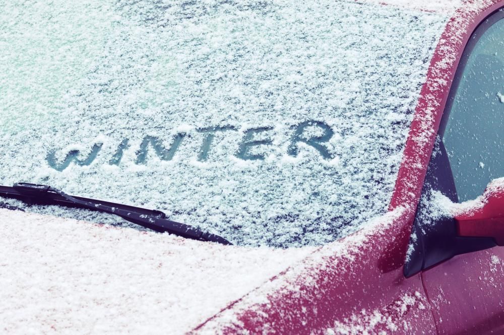 The word winter is written in the snow on the windshield of a red car