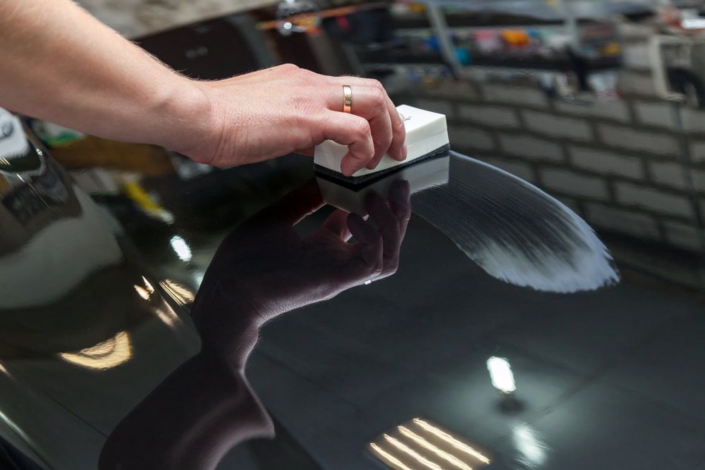 A person is polishing the hood of a car with a sponge.