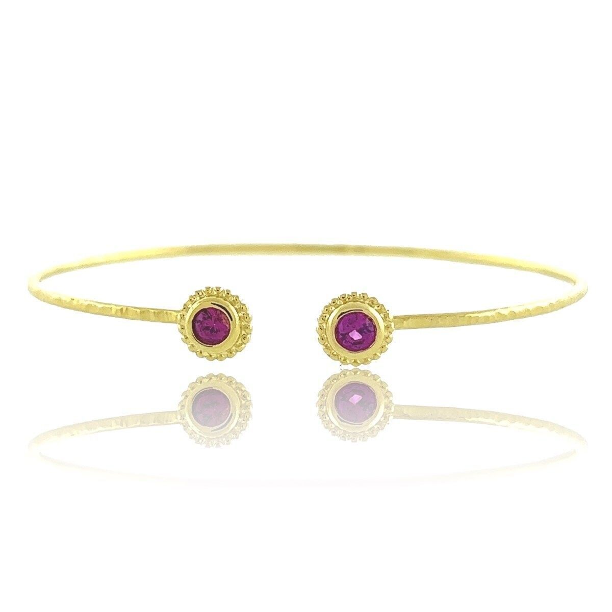 A gold bangle with two purple stones on a white background.