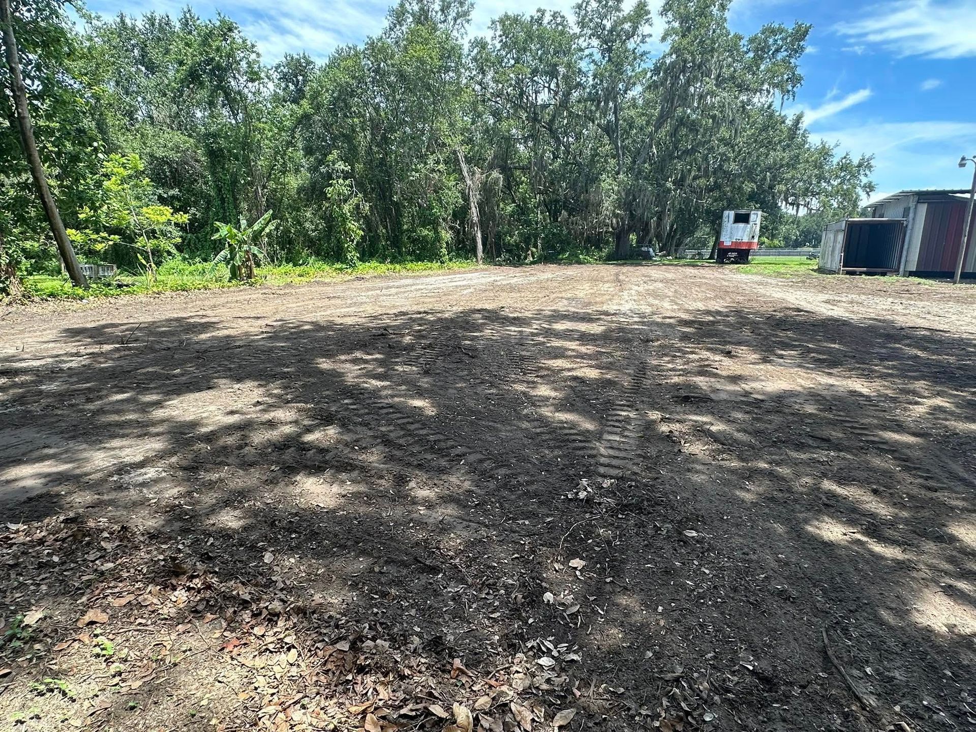 Cleared gravel lot with trees in the background, a small truck, and cargo containers on the right.