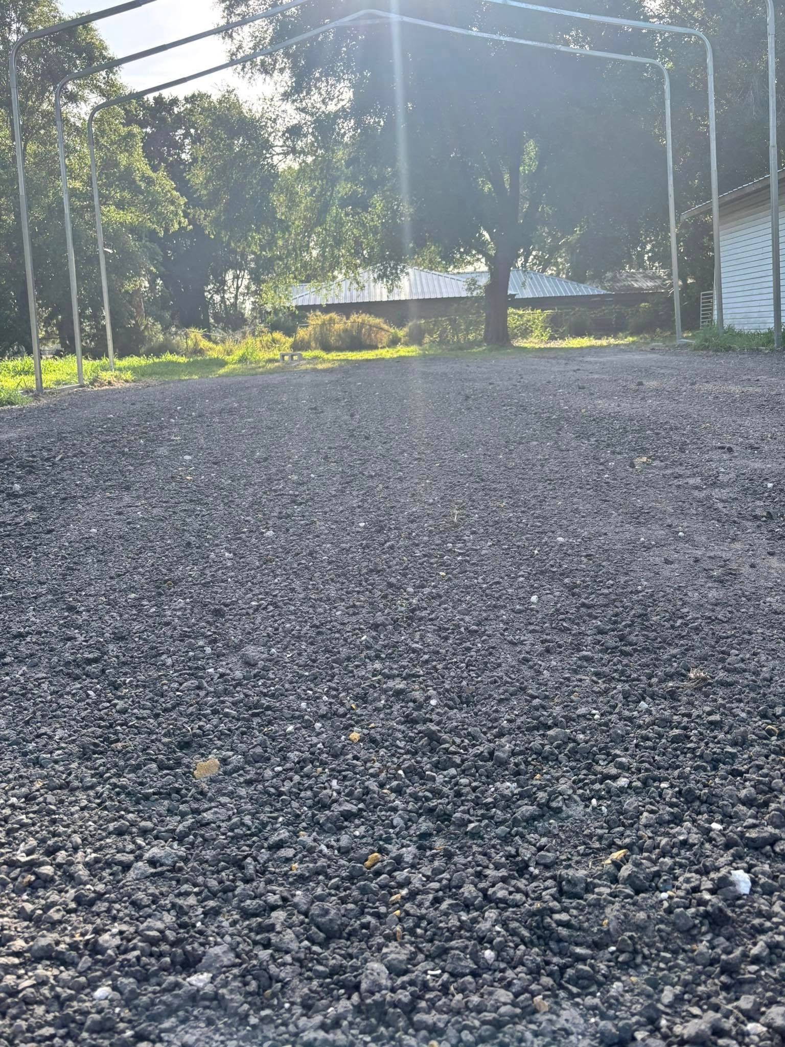Gravel surface with metal framework, trees, and sunlight.