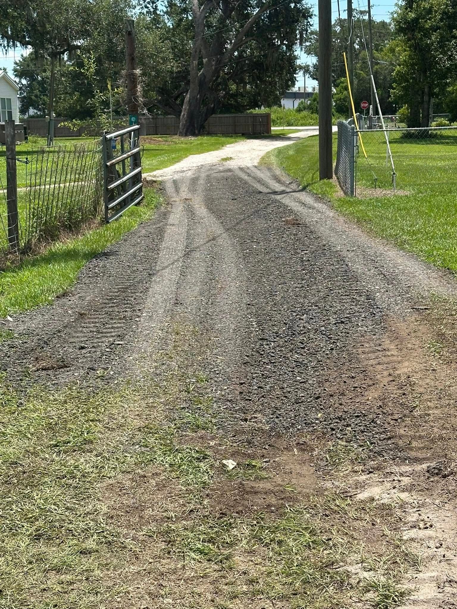 Gravel driveway leading towards a house, flanked by grass and a gate.