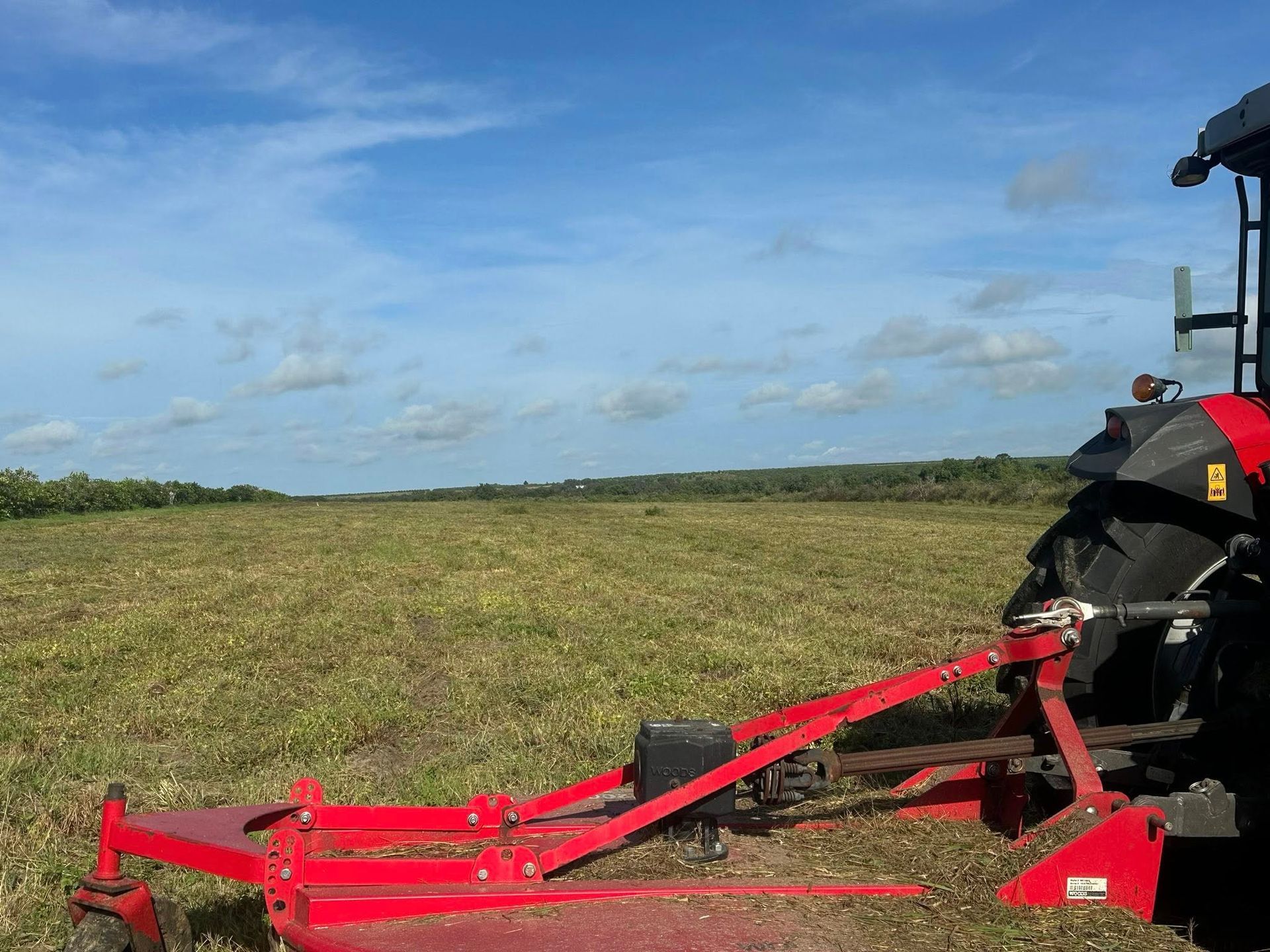 Red tractor mowing a field under a blue sky.