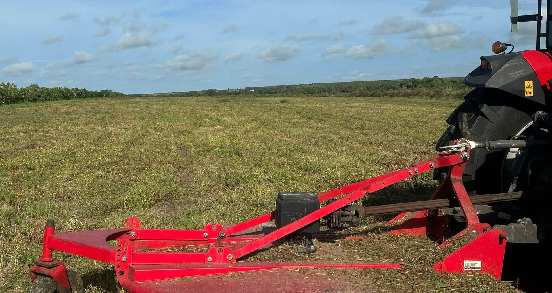 Red tractor pulling a mower across a field on a sunny day.