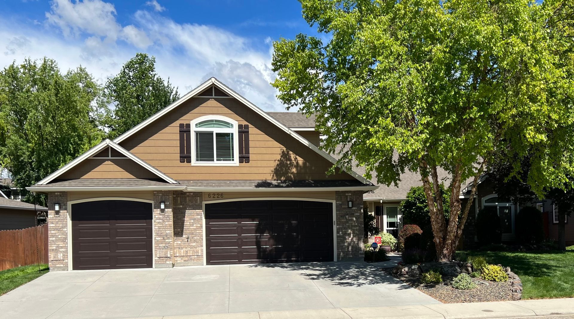 A large house with two garages and a tree in front of it.