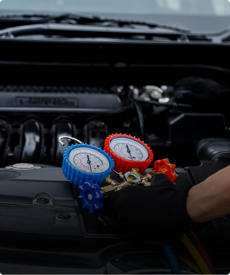Mechanic in blue gloves working on orange car engine with a tool. | Las Truck & Auto