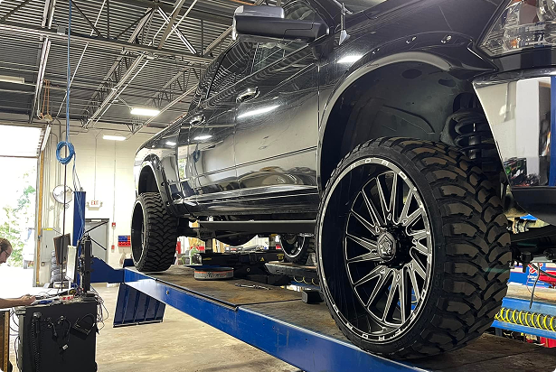 Black pickup truck on a lift in a garage, showcasing large custom wheels and tires. | Las Truck & Auto