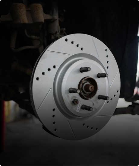 Drilled and slotted silver brake rotor on a car, ready for installation. | Las Truck & Auto