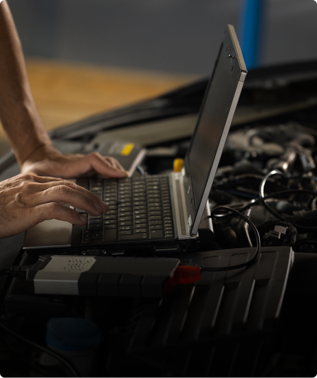 Hands typing on a laptop connected to a car engine, likely performing diagnostics in a garage. | Las Truck & Auto