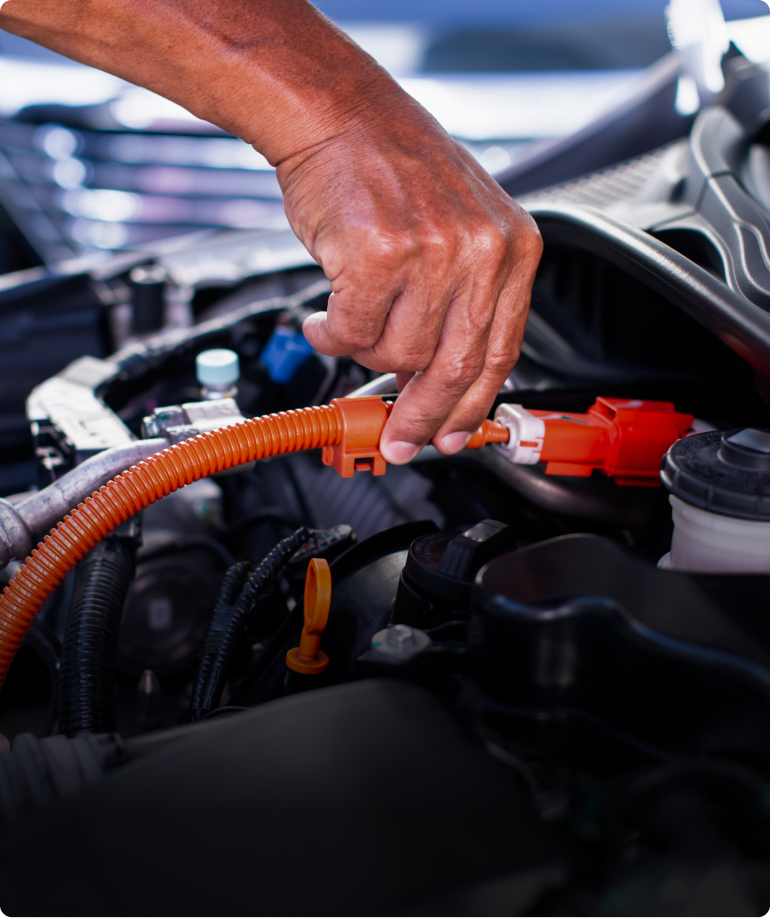 Hand connecting orange cable in car engine compartment. | Las Truck & Auto