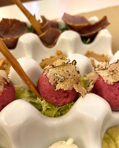 Antipasto di conchiglie di capesante bianche guarnite con palline di gelato rosa e verdi e decorazioni a scaglie, infilzate su spiedini di legno.