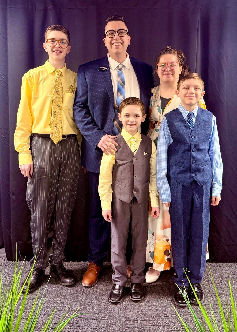 Five people stand together posing indoors, dressed in formal and bright clothes.