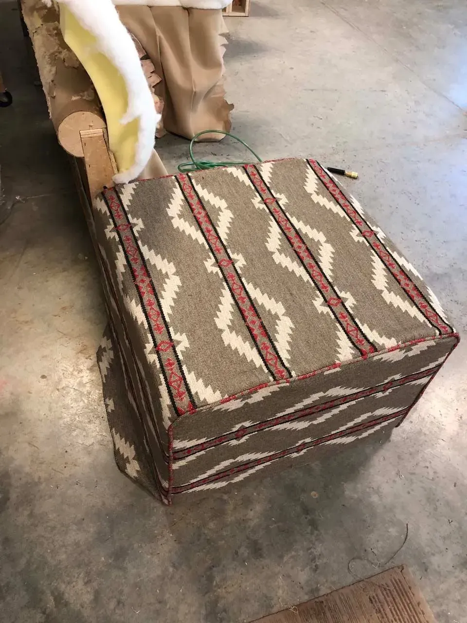 An ottoman with a pattern on it is sitting on a concrete floor.