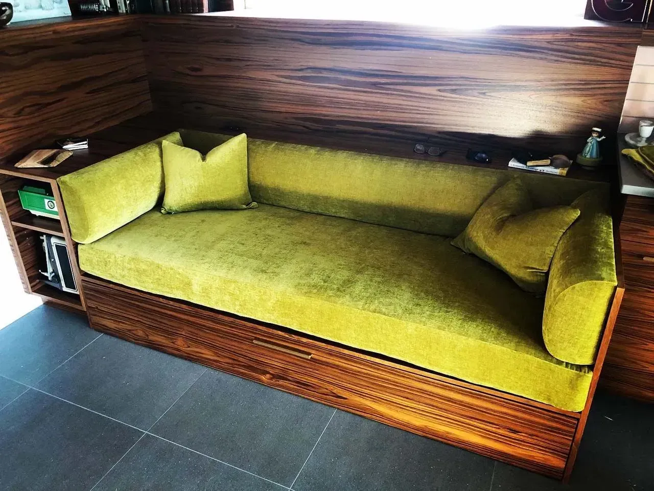 A green couch is sitting in a room next to a window.