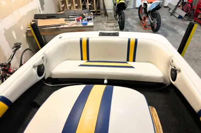 A boat with a yellow and blue stripe on the seat is in a garage.